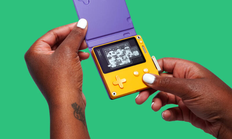 The playdate console's black and white screen is shown - a person is holding the console between their hands